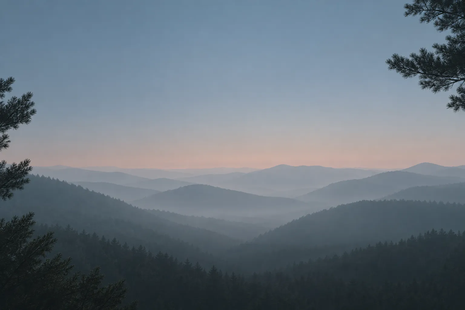 Fogged mountain ridgelines receding into pale blue-grey haze at dawn, framed by dark conifer branches at the corners